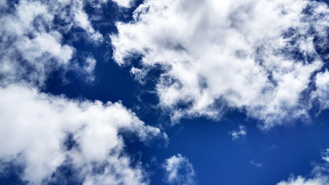 a plane flying through a cloudy blue sky, by Niko Henrichon, precisionism, fluffy white clouds, looking up, vibrant blue, profile image
