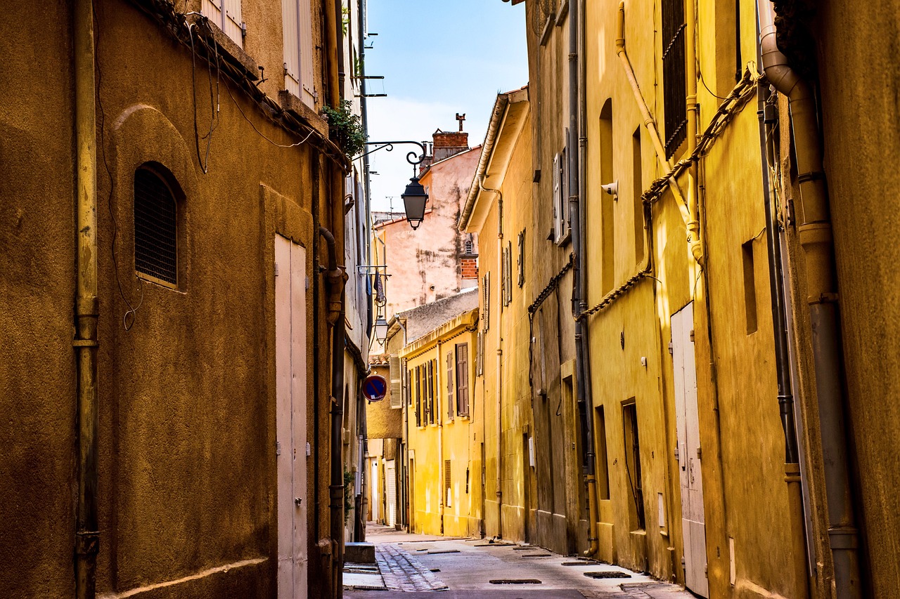 a narrow street in an old european city, a picture, by Raphaël Collin, shutterstock, shades of yellow, sand - colored walls, complex background, nice afternoon lighting