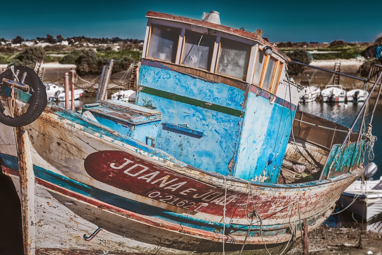 a boat sitting on top of a beach next to a body of water, a colorized photo, by Juan Carlos Stekelman, pixabay contest winner, photorealism, peeling paint, portrait of an old, joshua cotter, fishing village