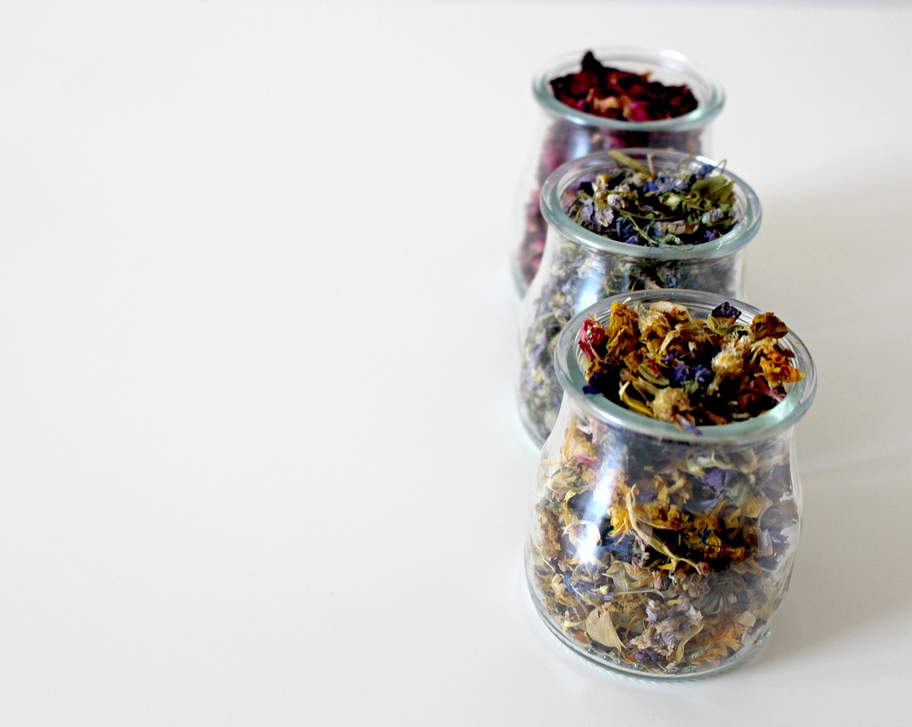 three glass jars filled with dried flowers on a white surface, a picture, high quality product photo, teapots, high res photo, with beautiful colors