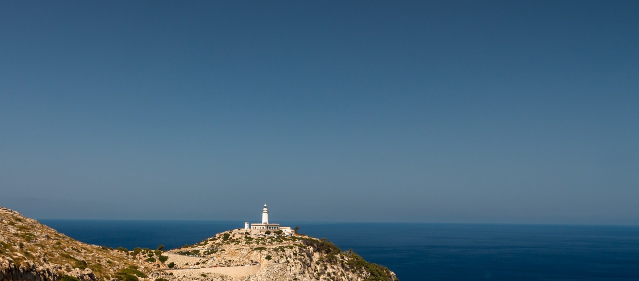 a lighthouse sitting on top of a mountain next to the ocean, a picture, inspired by Fede Galizia, minimalism, ibiza, shot on nikon d 3 2 0 0, clear blue skies, josh grover