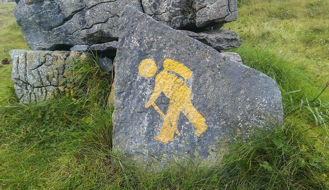 a rock with a yellow sign on it, a cave painting, inspired by Ada Hill Walker, man walking, celtic art, hiking cane, celtics