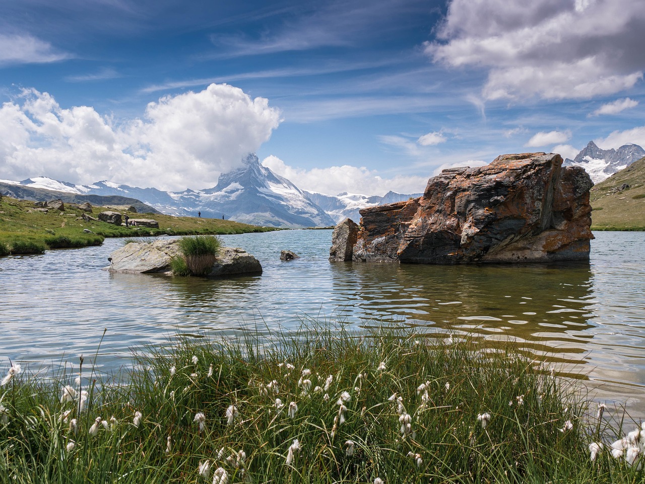 a large rock in the middle of a body of water, by Werner Andermatt, shutterstock, mountain behind meadow, high quality photos, beautiful summer landscape, very detailed picture