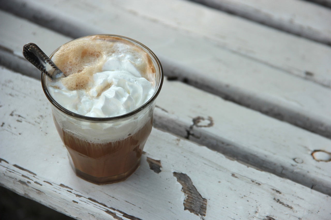 a cup of coffee with whipped cream and a spoon, outside, layered, soda, on a wooden table