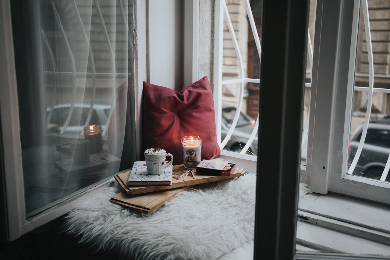a cup of coffee sitting on top of a window sill, romanticism, books on side table, room full of candles, connection rituals, inside a cozy apartment