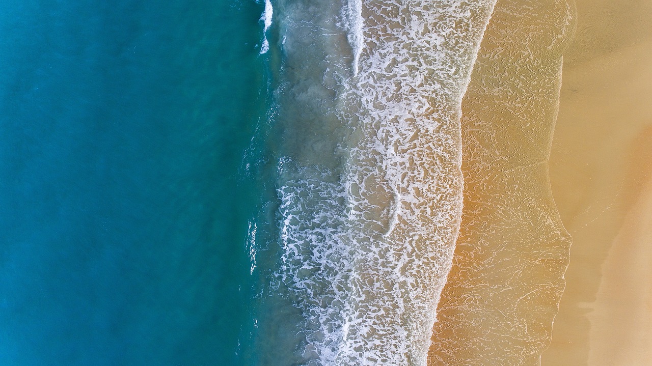 a person riding a surfboard on top of a sandy beach, by Etienne Delessert, pexels, minimalism, color aerial photo drone, 4k vertical wallpaper, yellow and blue and cyan, closeup 4k