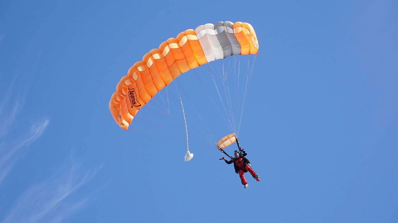 a person that is in the air with a parachute, orange and white color scheme, the photo shows a large, tan, sport