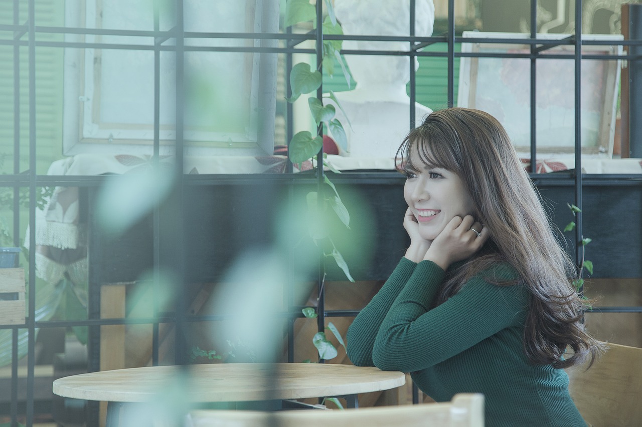 a woman sitting at a table with her hand on her chin, a picture, inspired by Kim Jeong-hui, wearing a green sweater, happy cozy feelings, lalisa manobal, f2.8 35mm