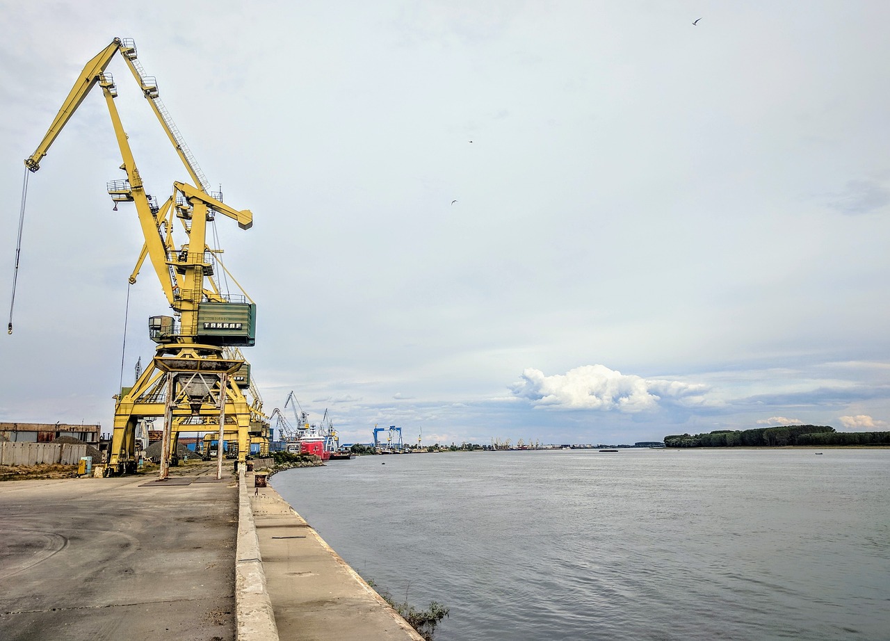 a large crane sitting next to a body of water, a picture, by Ilya Ostroukhov, shutterstock, port scene background, long view, rutkowskyi, taken on iphone 14 pro