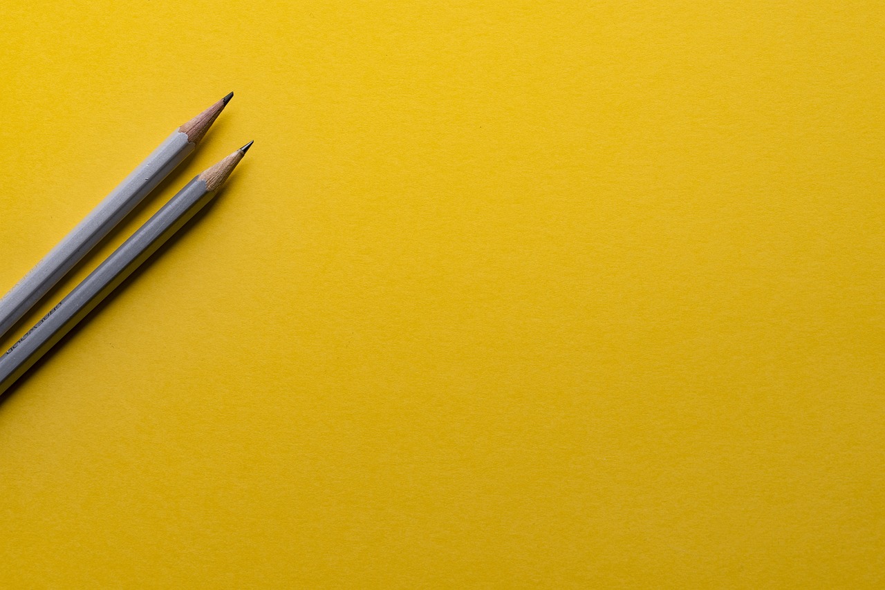 two pencils sitting next to each other on a yellow surface, by Richard Carline, pexels, minimalism, banner, graphite, a wide shot, solid background color