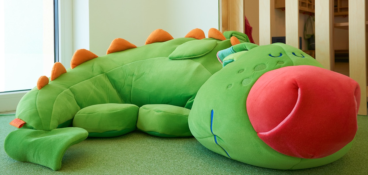 a stuffed dragon laying on the floor next to a window, inspired by Otakar Sedloň, softplay, large couch, detail shot, green dragon