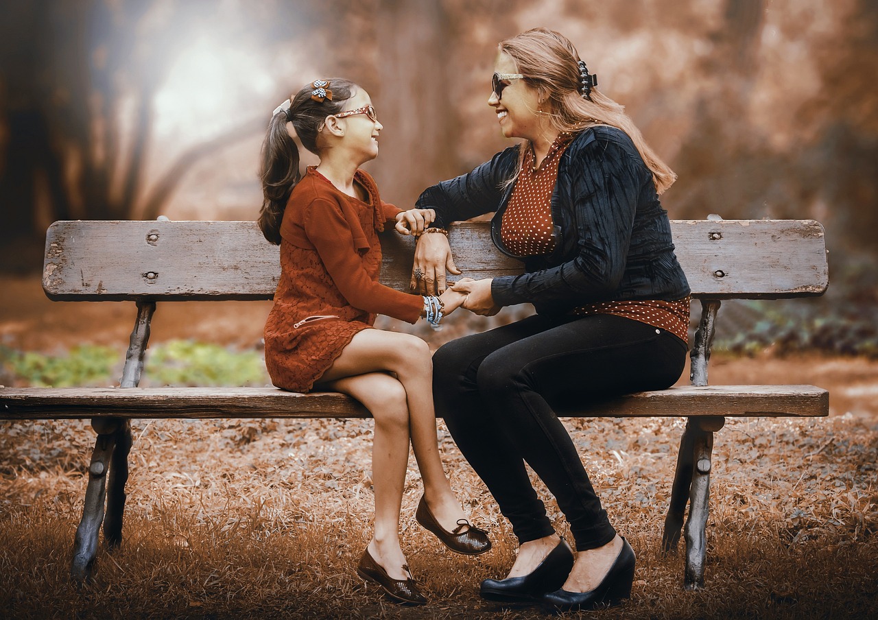 a couple of women sitting on top of a wooden bench, a picture, pexels, digital art, mom, daughter, interacting and posing, holding hands