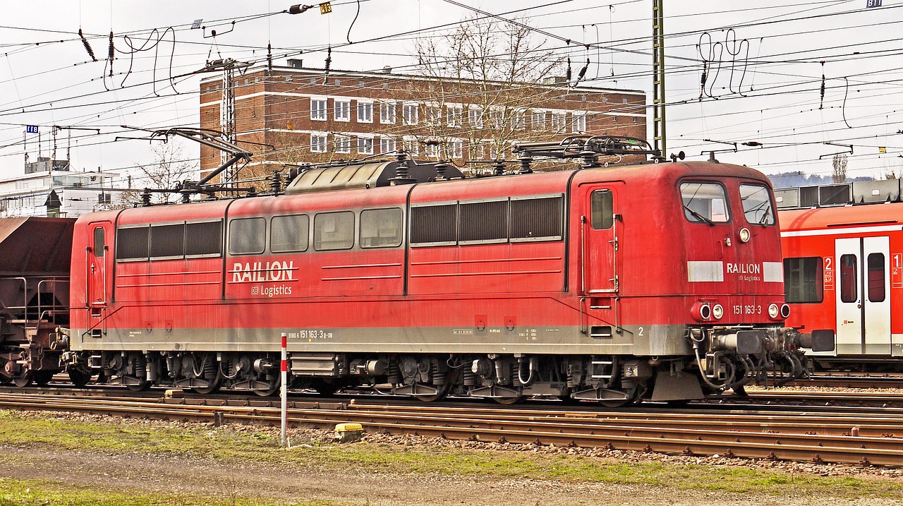 a red train traveling down train tracks next to a tall building, a portrait, by Karl Hagedorn, flickr, baroque, panoramic, well worn, april, img_975.raw