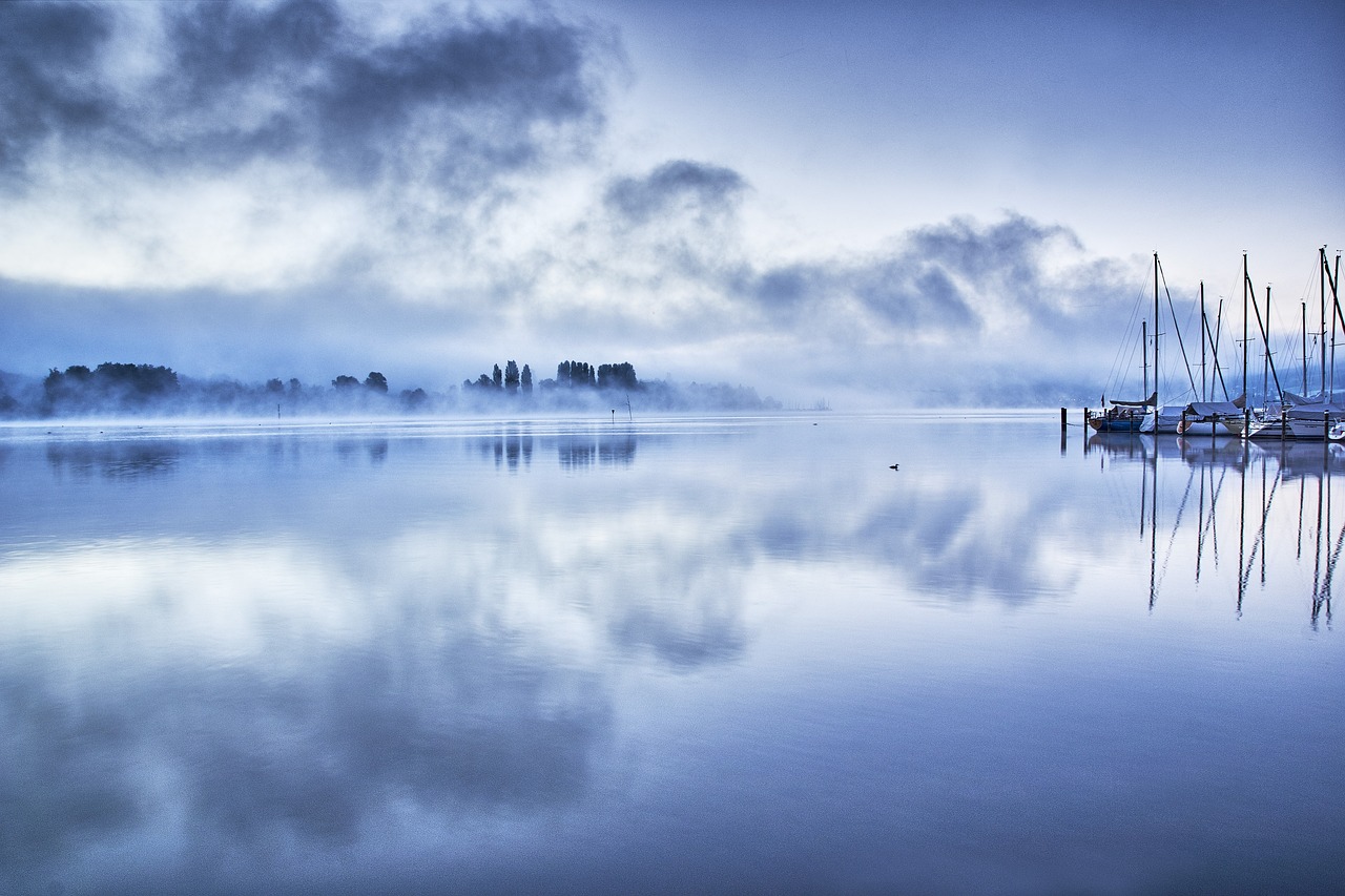a group of boats floating on top of a lake, a photo, by Andrew Geddes, flickr, romanticism, blue mist, panoramic photography, beautiful morning, new zeeland