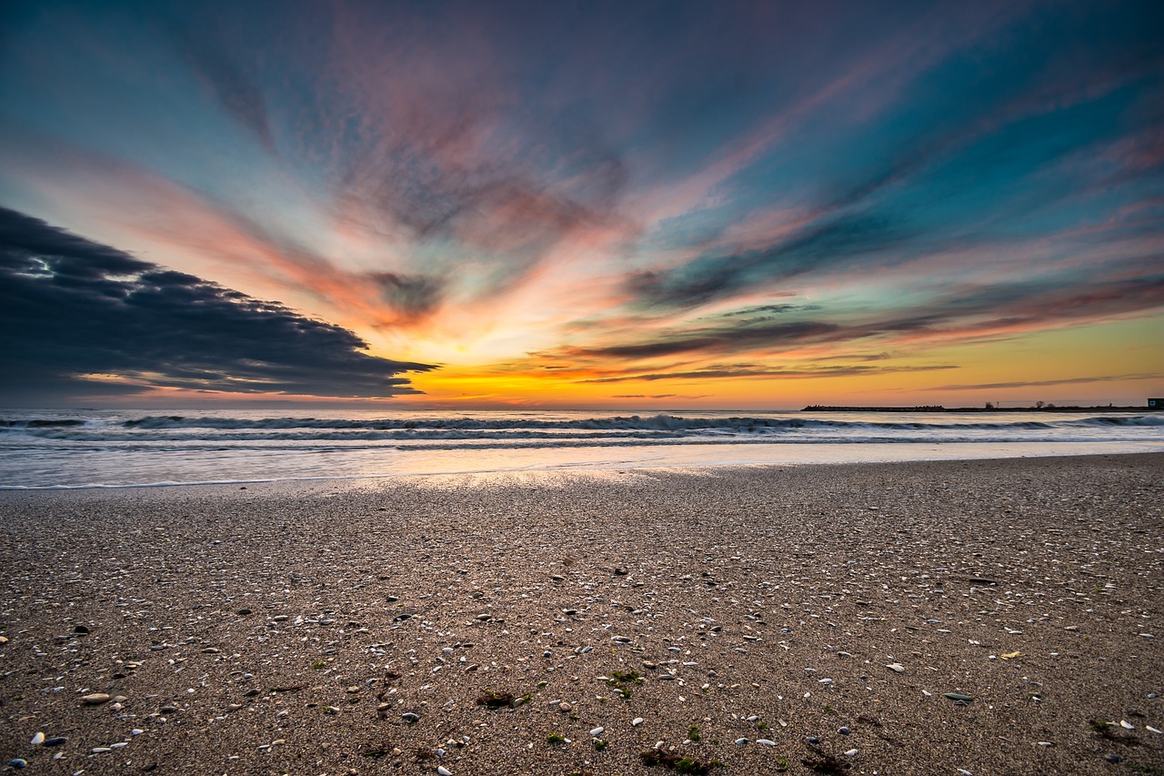 a large body of water sitting on top of a sandy beach, a picture, shutterstock, vibrant sunset dramatic sky, cornwall, highly detail wide angle photo, colorful swirly magical clouds