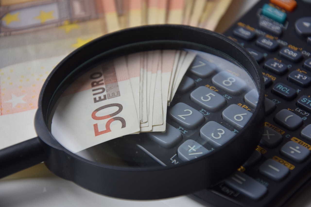 a magnifying glass sitting on top of a calculator, a photo, by Mathias Kollros, shutterstock, photorealism, zoomed view of a banknote, set photo, iso 50, stock photo