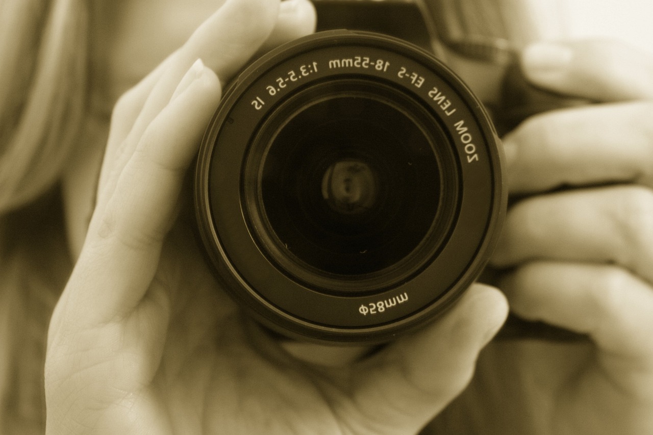 a close up of a person holding a camera, a picture, sepia, zoom lens, !! looking at the camera!!, cameras lenses
