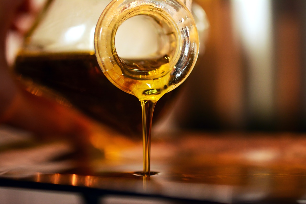 a glass filled with liquid sitting on top of a table, a photorealistic painting, shutterstock, hyperrealism, cooking oil, shallow depth of focus, honey, pouring