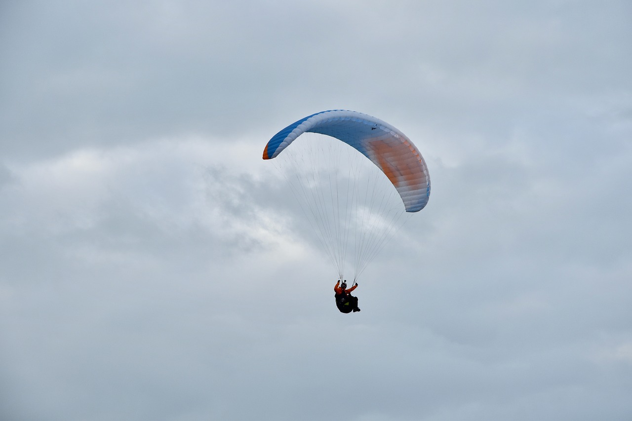 a person that is in the air with a parachute, a picture, overcast weather, buggy, strong blue and orange colors, wide shot photo