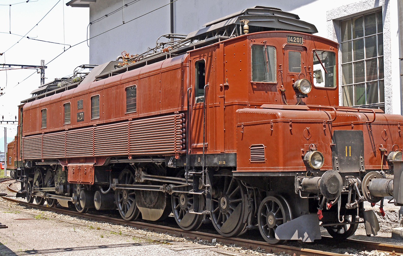 a red train traveling down train tracks next to a building, by Sigmund Freudenberger, flickr, stained antique copper car paint, diesel engine, profile picture 1024px, alps