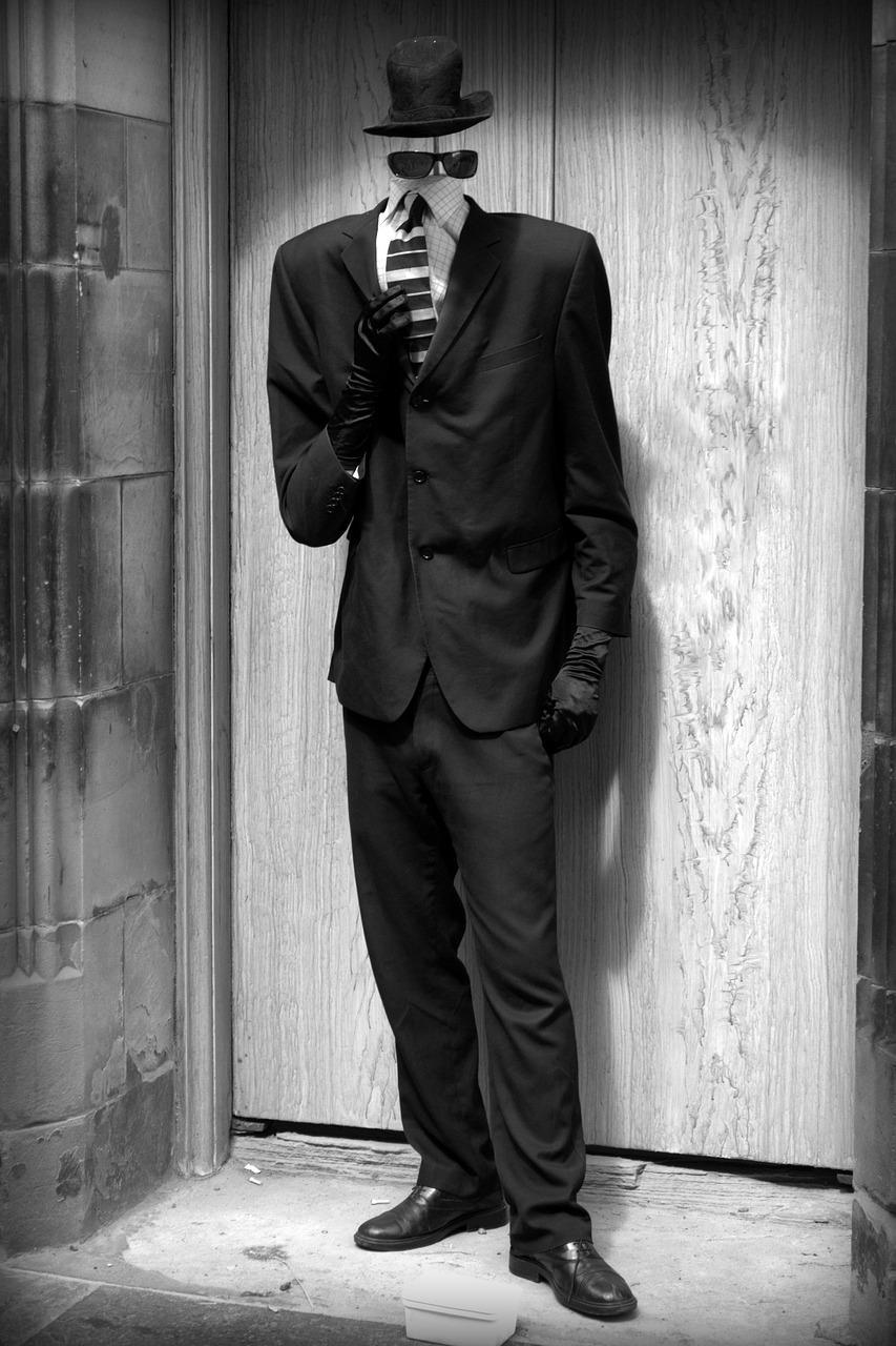 a black and white photo of a man in a suit and tie, a black and white photo, inspired by August Sander, flickr, bauhaus, zentai suit, wearing modern gothic clothes, leaning on door, photo in style of tyler mitchell