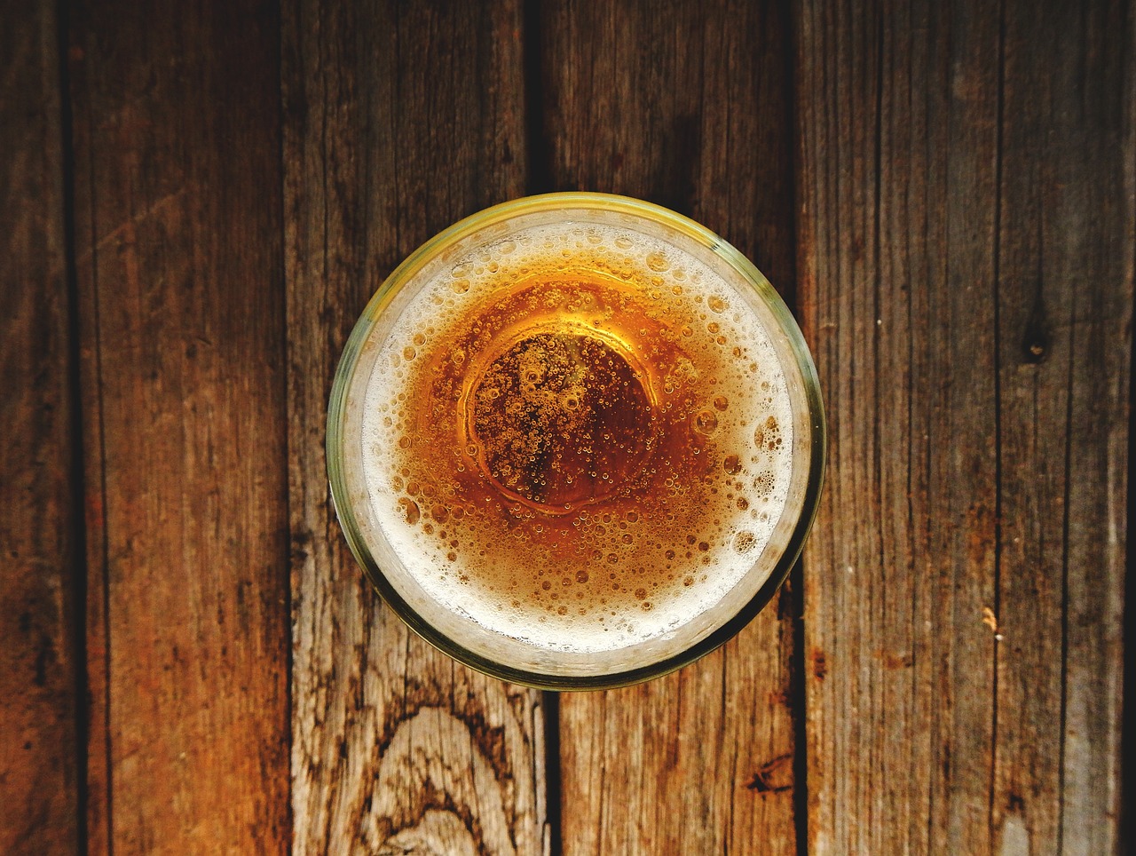 a glass of beer sitting on top of a wooden table, a digital rendering, pexels, view from above, round-cropped, battered, wall