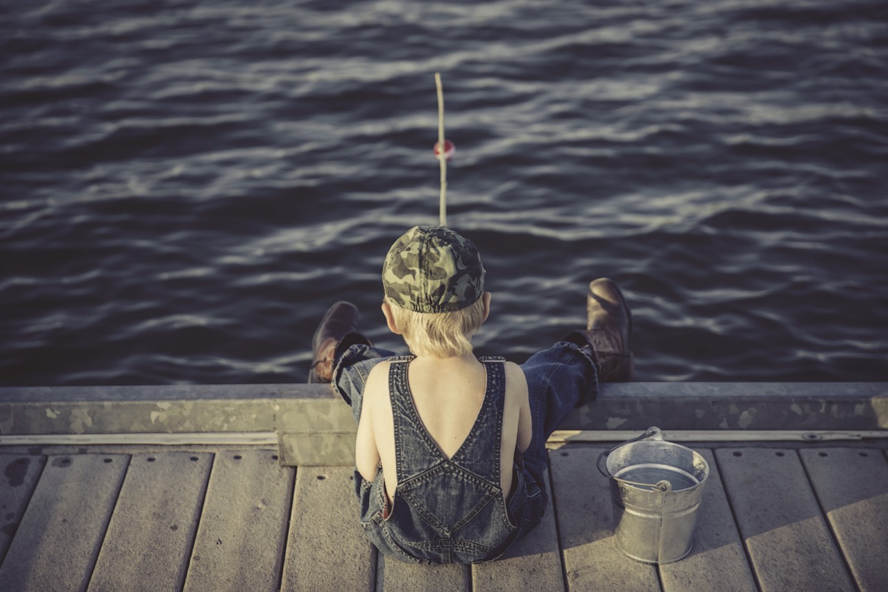 a person sitting on a dock with a fishing rod, a picture, pexels, kid, waiting, wearing a straw hat and overalls, future activist