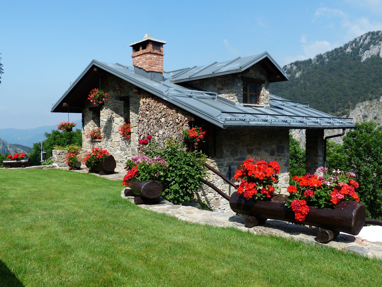 a house sitting on top of a lush green hillside, decorated with flowers, stone roof, pristine and clean design, exterior photo