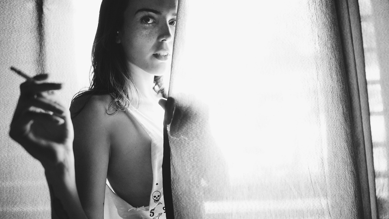 a black and white photo of a woman holding a cigarette, by Amelia Peláez, diffuse natural sun lights, wearing white camisole, discreet lensflare, leaning against the window