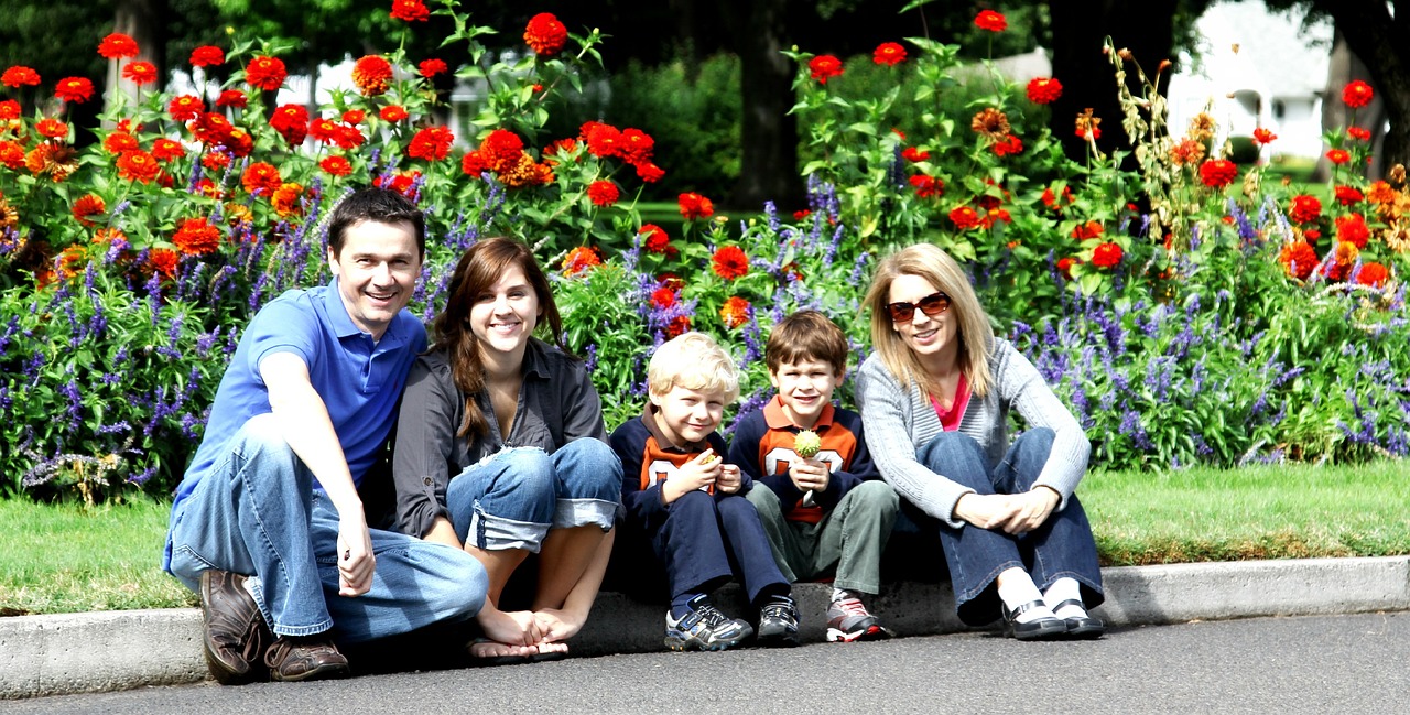 a group of people sitting on the side of a road, inspired by Thomas Struth, realism, flowers in background, husband wife and son, taken in zoo, july 2 0 1 1