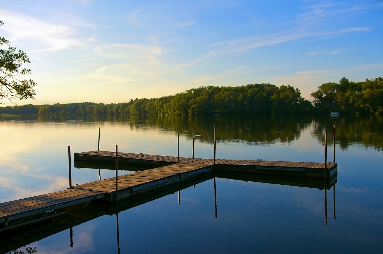 a dock sitting on top of a lake next to a forest, illinois, peaceful evening harbor, a photo of a lake on a sunny day, video