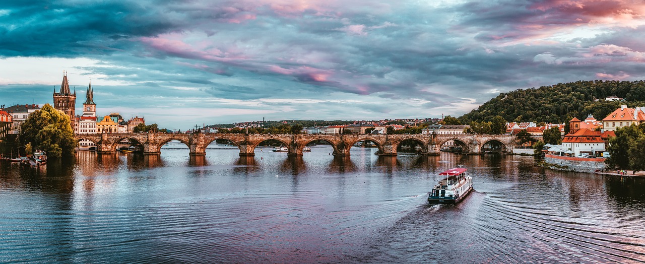 a boat traveling down a river next to a bridge, by Gabor Szikszai, pexels contest winner, romanticism, panoramic, pink clouds, prague, body