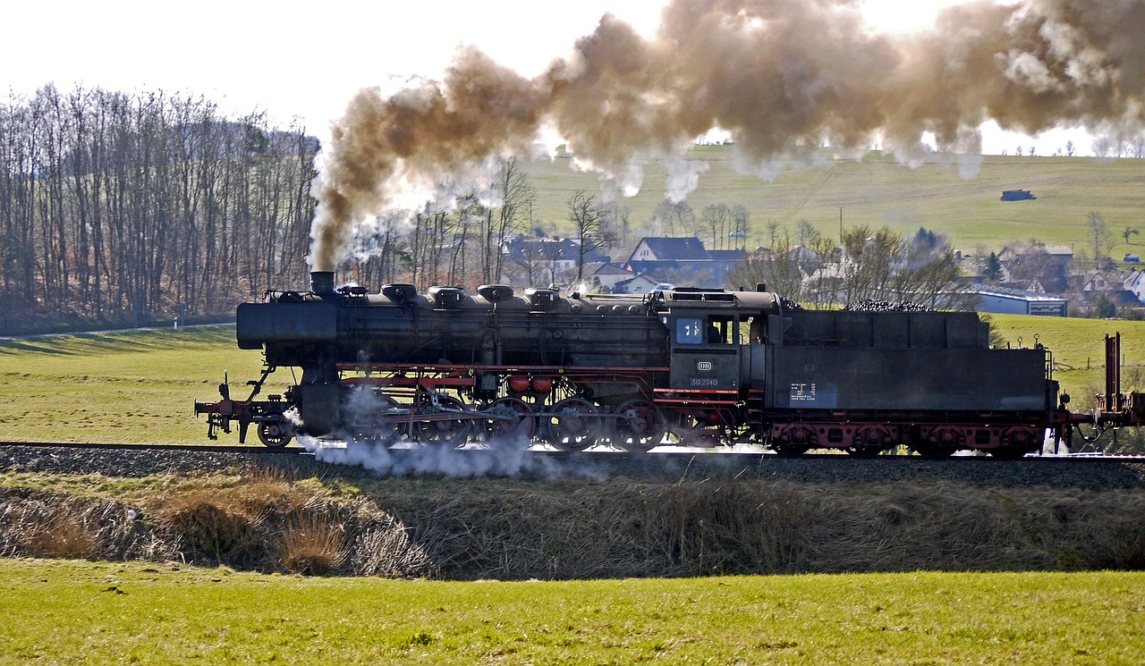 a train traveling down train tracks next to a lush green field, a portrait, by Jörg Immendorff, flickr, brass and steam technology, blowing out smoke, big engine, february)