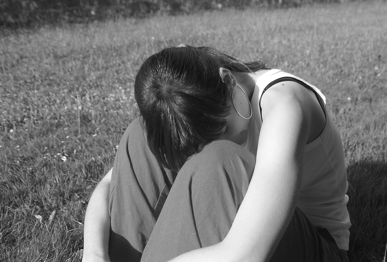 a black and white photo of a woman sitting in the grass, pixabay, realism, hugging, taken in the late 2000s, self deprecating, seen from the back