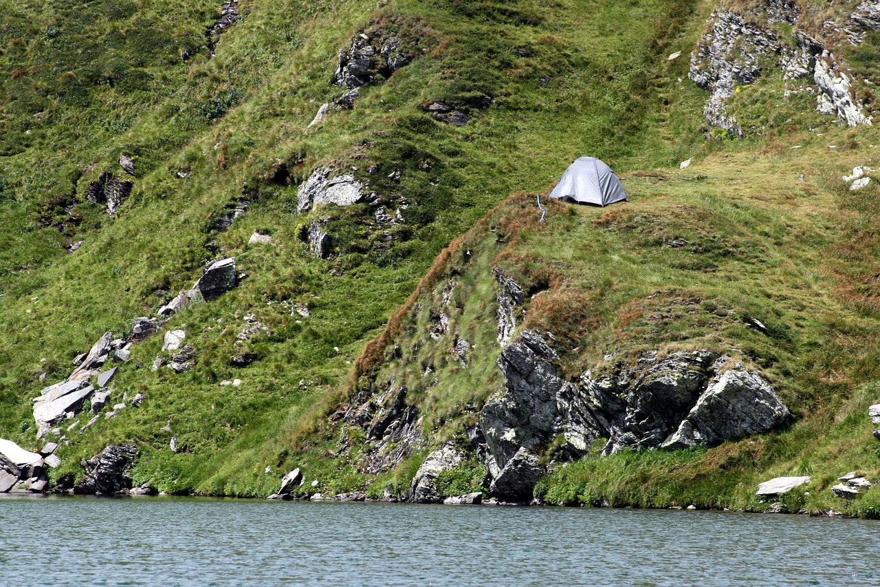 a tent sitting on top of a lush green hillside, a photo, by Werner Andermatt, shutterstock, partly sunken! in the lake!, detailed zoom photo, grey, tourist photo