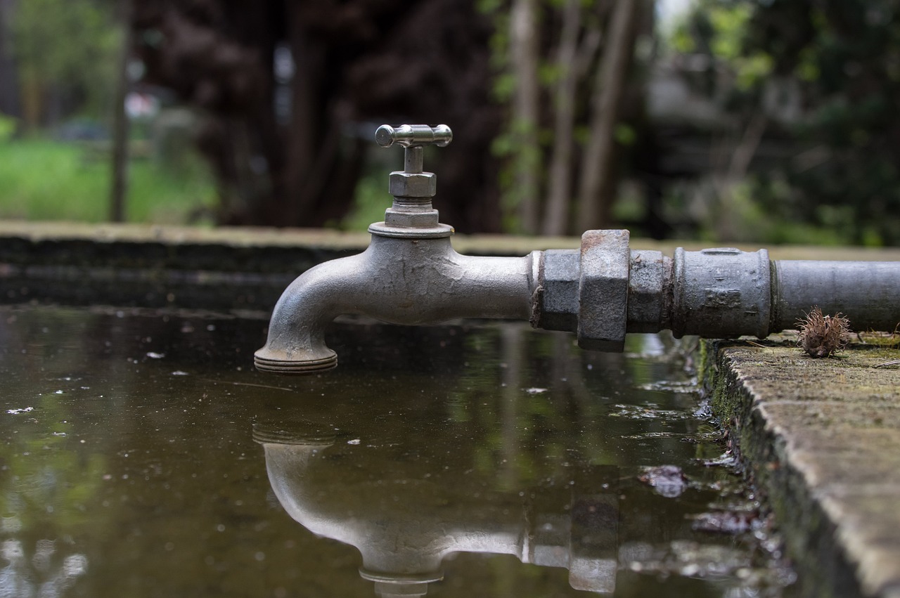 a metal faucet sitting on top of a puddle of water, a tilt shift photo, portlet photo