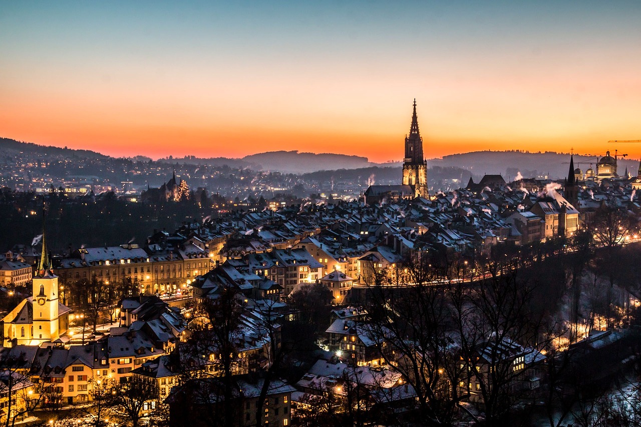 a view of a city from the top of a hill, by Karl Stauffer-Bern, shutterstock, dark winter evening, warm glow, tourist photo, spire