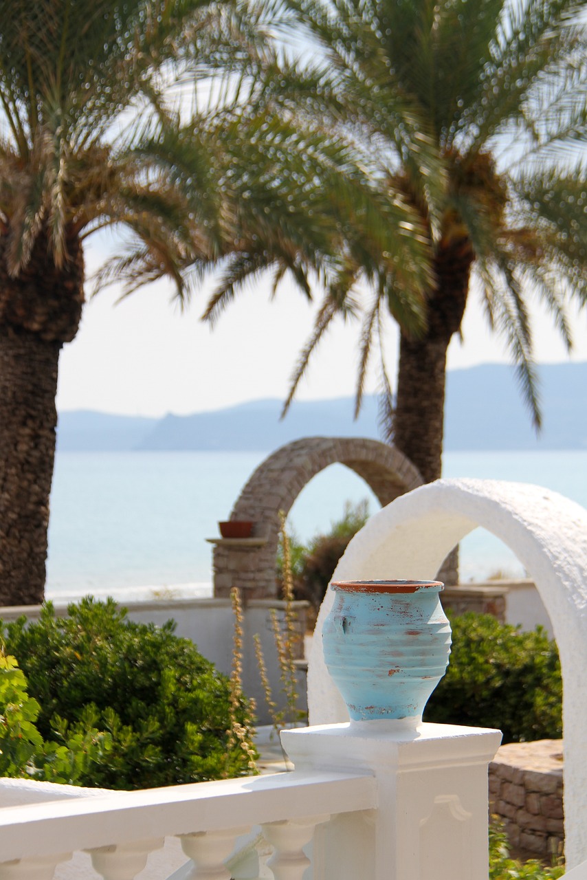 a blue vase sitting on top of a white fence, inspired by Exekias, romanticism, palm trees on the beach, the sea in the background, amphora, high res photo