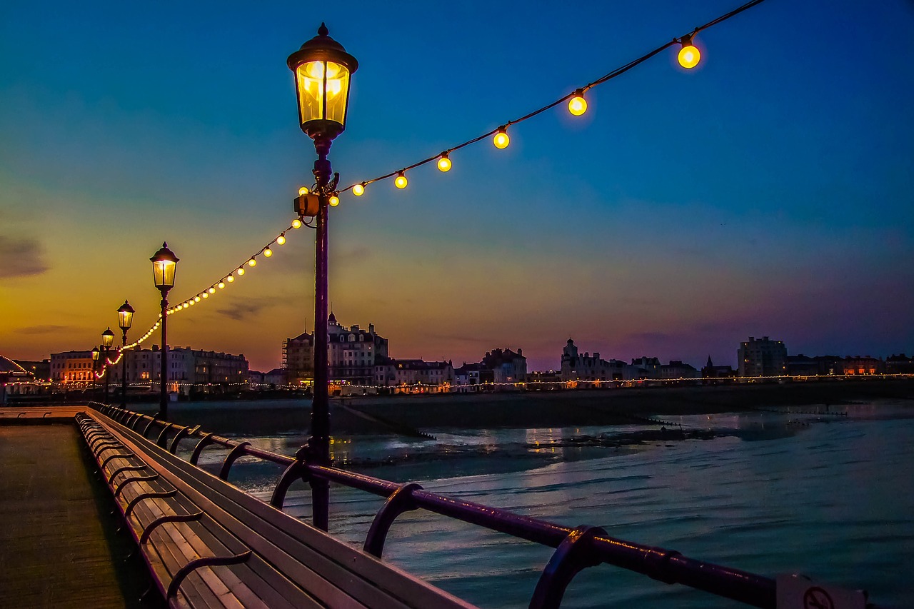 a bench sitting on top of a pier next to a body of water, a picture, by Raymond Coxon, shutterstock, romanticism, evening lanterns, victoriana, coast, streetlight