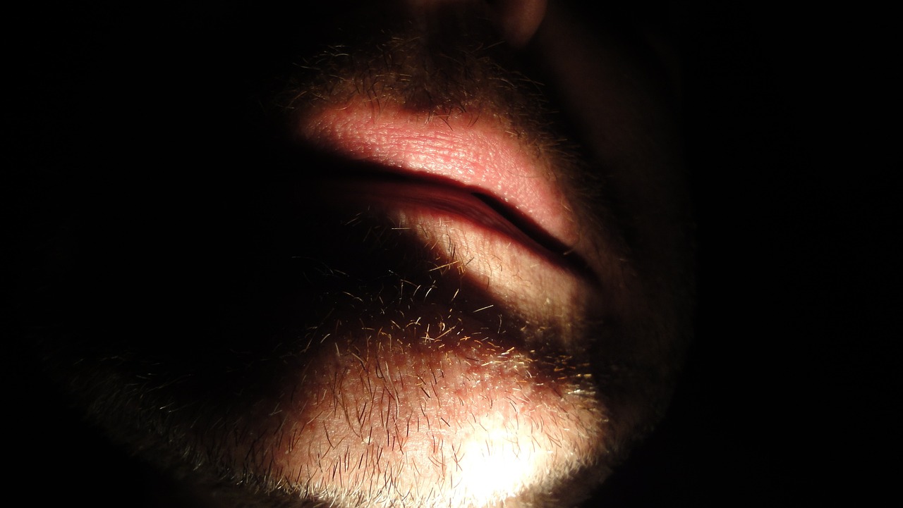 a close up of a man's face in the dark, by Jan Rustem, licking, unkempt beard, hyperrealistic flickr:5, discreet lensflare