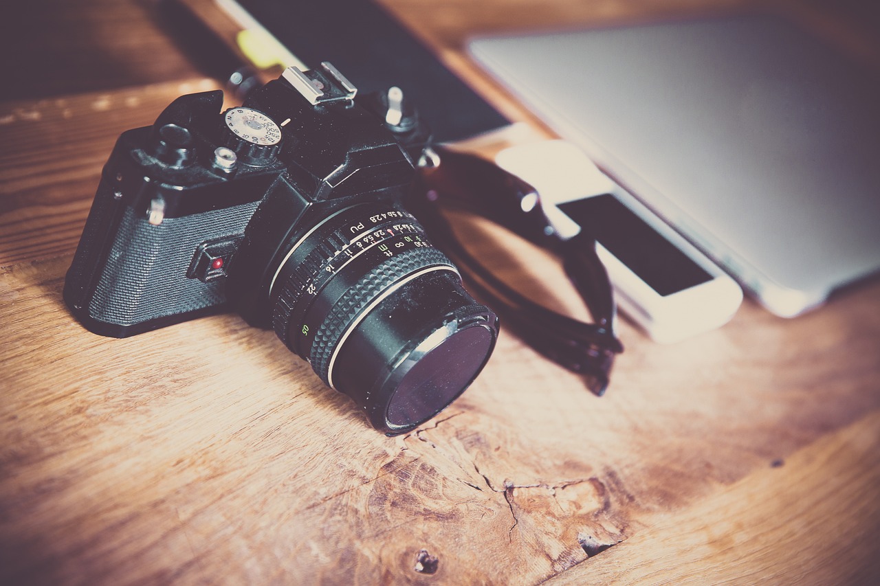 a camera sitting on top of a wooden table next to a laptop, a picture, art photography, cameras lenses, retro photography, lensflare, photorealism. trending on flickr