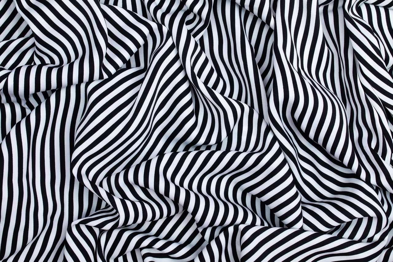 a close up of a black and white striped fabric, an abstract drawing, inspired by Bridget Riley, shutterstock, flowing silk sheets, dazzle camouflage, high quality product image”