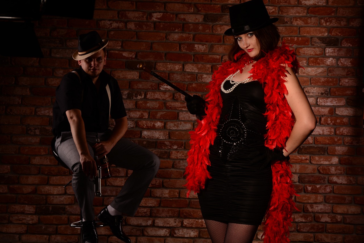 a woman standing next to a man in front of a brick wall, harlem renaissance, cosplay on black harley queen, 1920s studio lighting, background image, scarlet feather boa