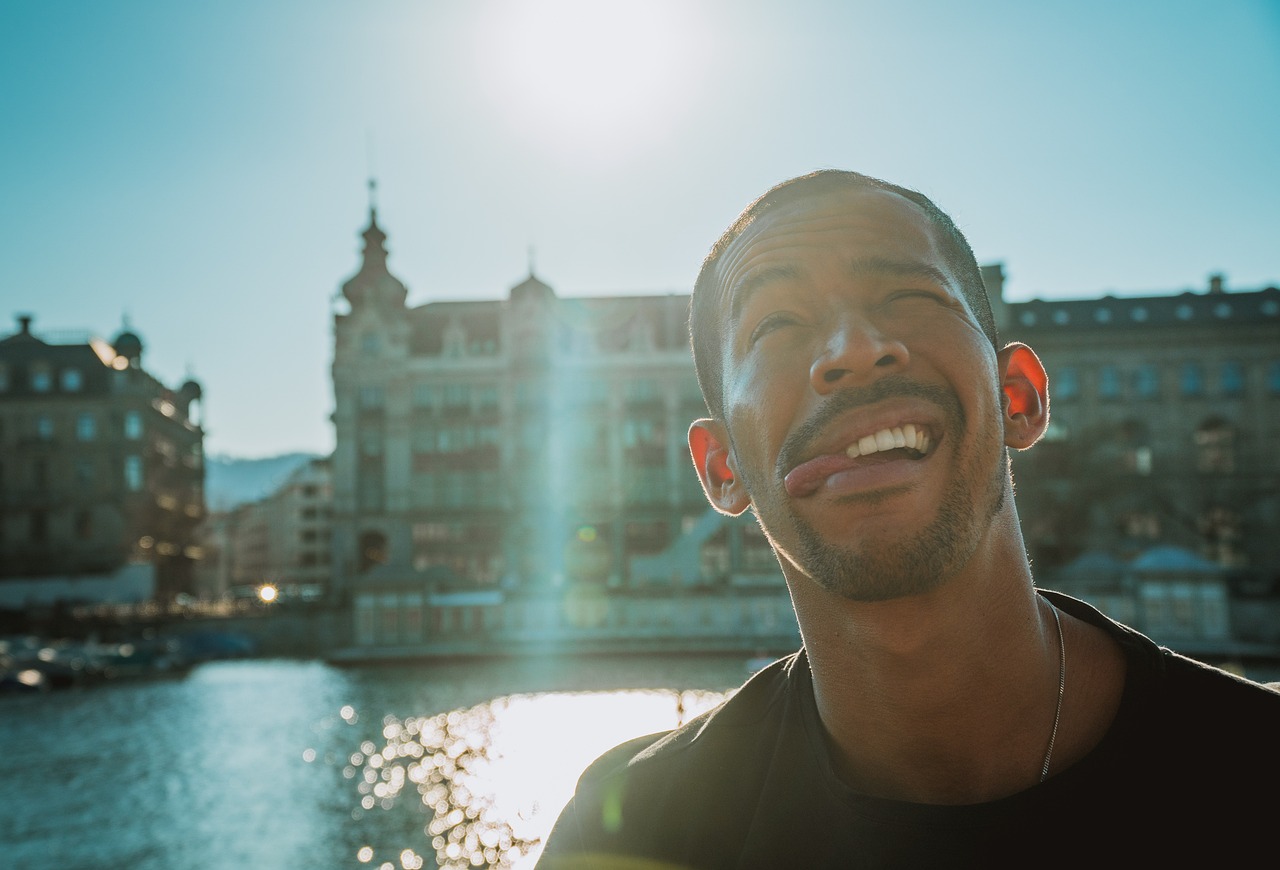 a man standing in front of a body of water, by Jakob Gauermann, large black smile, surrounding the city, having fun in the sun, drake's face