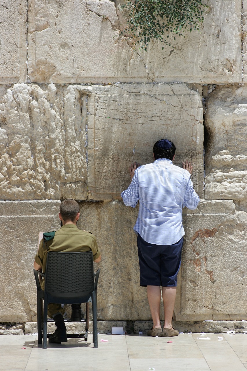 a man and a woman standing in front of a stone wall, a picture, by Elias Goldberg, pexels, the western wall, man sitting facing away, with a kid, as well as scratches