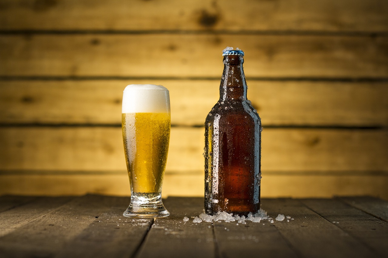a glass of beer next to a bottle of beer, shutterstock, on wooden table, blue liquid and snow, soft warm light, glass bottle