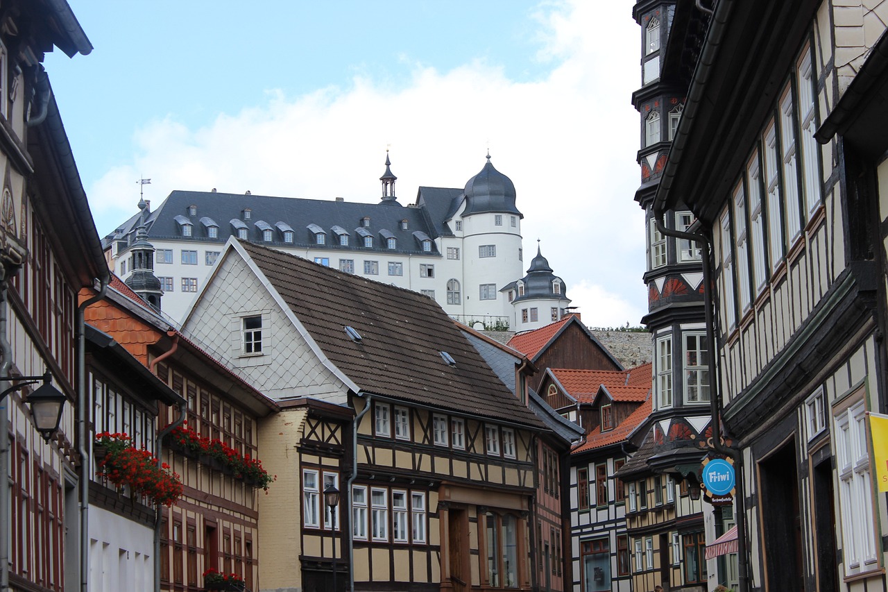 a group of people walking down a street next to tall buildings, a photo, heidelberg school, medieval house, turrets, log houses built on hills, portlet photo