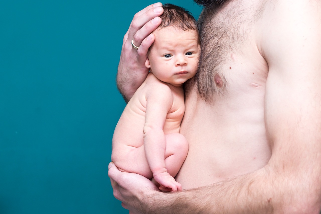 a man holding a baby in his arms, by Etienne Delessert, flickr, teal studio backdrop, belly button showing, 2014, potrait