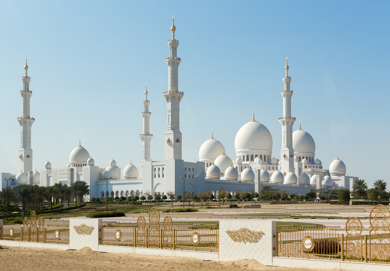 a large white building sitting in the middle of a desert, inspired by Sheikh Hamdullah, art nouveau, black domes and spires, pure gold pillars, grazing, gulf