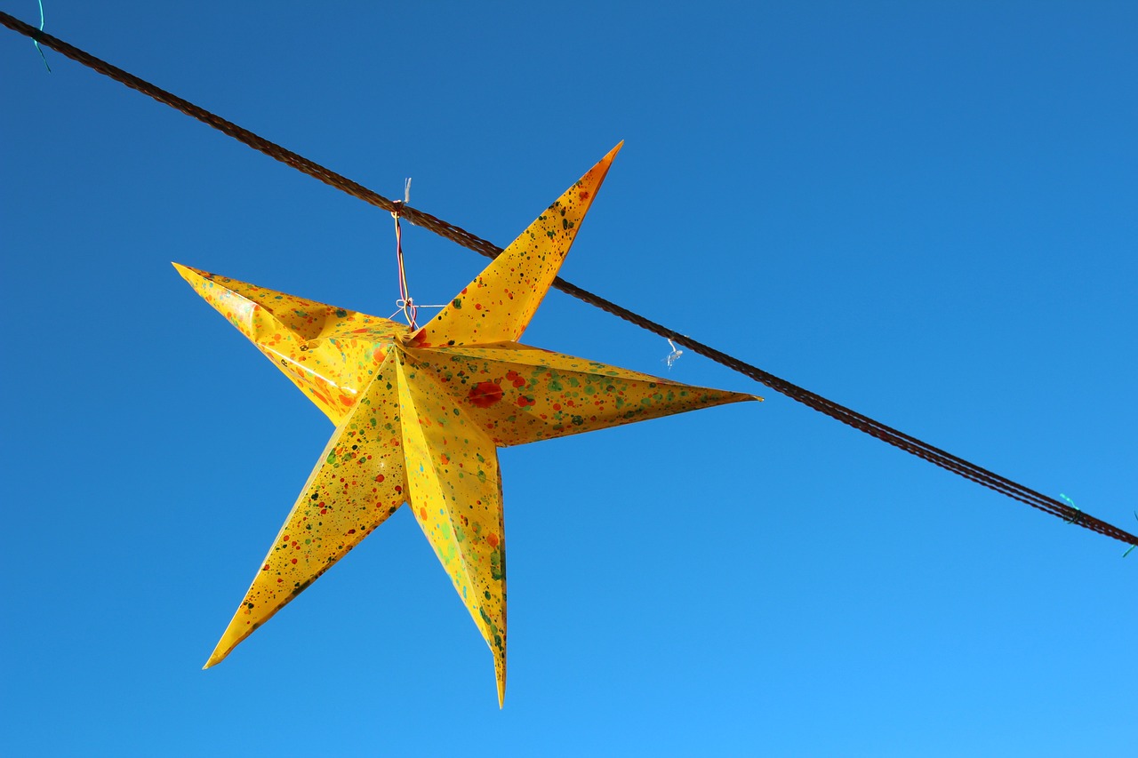 a yellow paper star hanging from a power line, a photo, folk art, in a sunny day, colorful stars, hyperdetailed, looking this way